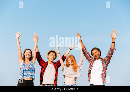 Multiethnische Gruppe glücklich Jugendlicher Stand mit erhobenen Händen über blauen Himmelshintergrund Stockfoto