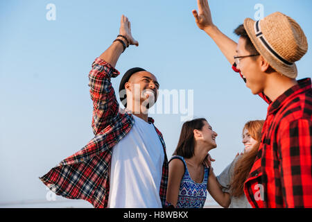 Fröhliche junge Freunde lachen und geben hohe fünf im freien Stockfoto