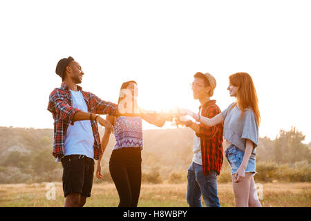 Multiethnische Gruppe von fröhlichen jungen Freunden stehen und trinken Bier und Erfrischungsgetränke im freien Stockfoto