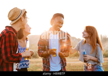 Gruppe von lächelnden jungen Freunden sprechen und trinken Bier und Erfrischungsgetränke im freien Stockfoto