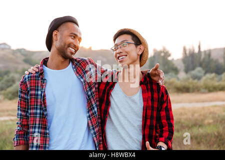 Zwei fröhliche asiatischen und afrikanischen amerikanischen jungen Freunde stehen zusammen im freien Stockfoto