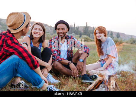 Gruppe der glückliche junge Menschen in der Nähe von Lagerfeuer beisammen sitzen Stockfoto