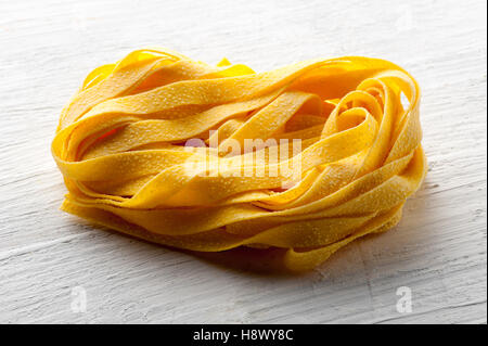 Roll der rohe italienische Tagliatelle Pasta oder Band Nudeln für traditionelle mediterrane Küche in einer Nahaufnahme auf einem weißen Holz Stockfoto