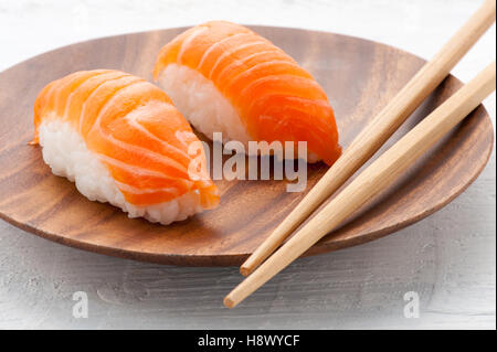 Zwei frische Lachs Nighiri Sushi auf einer Holzplatte mit Stäbchen serviert als Aperitif zum Abendessen Stockfoto