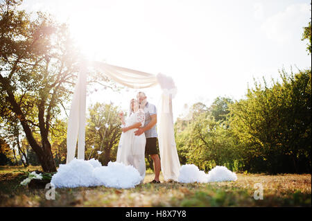 Glücklich schwanger paar bleiben umarmen und lieben in der Nähe von Dekor Bogen am Garten auf sonnigen Tag. Stockfoto