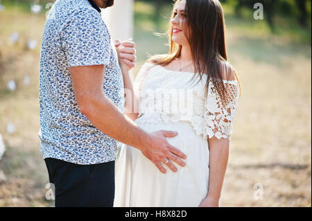 Glücklich schwanger paar bleiben umarmen und lieben in der Nähe von Dekor Bogen am Garten auf sonnigen Tag. Stockfoto