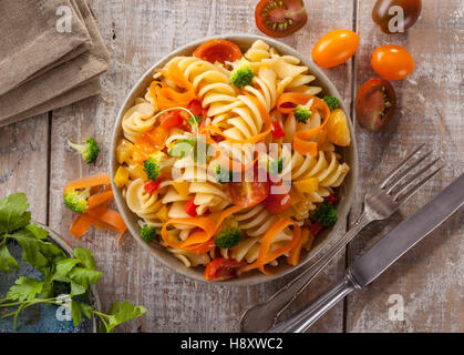 Fusilli Nudeln mit bunten Tomaten, Karotten und Brokkoli auf einem weißen Holztisch italienische Küche. Stockfoto