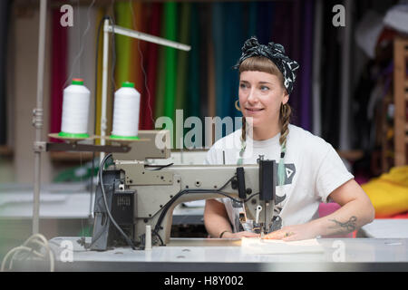 Junge tätowierte Schneiderin Nähen in einer Fabrikumgebung Stockfoto