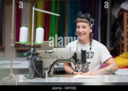 Junge tätowierte Schneiderin Nähen in einer Fabrikumgebung Stockfoto