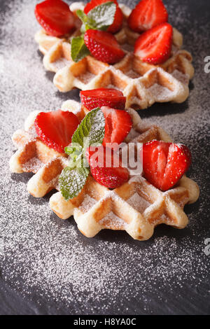 Waffeln mit frischen Erdbeeren und Minze, bestreut mit Puderzucker Nahaufnahme auf der Schiefertafel. vertikale Stockfoto