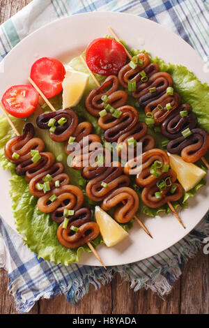 Kebab aus Calamari auf Spieße mit Gemüse auf einem Teller. vertikale Ansicht von oben Stockfoto