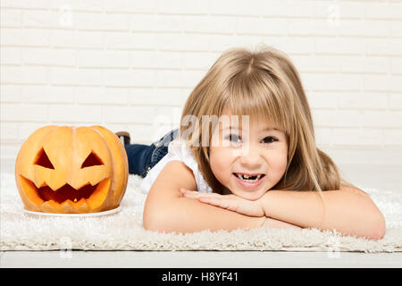 Lächelndes Kind Mädchen in Windeln mit Kürbis am Boden liegend. Vorbereitung für Halloween. Stockfoto