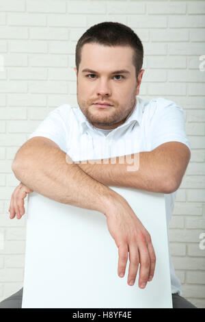 Mann mittleren Alters mit gepflegten Bart, beim Sitzen in der Nähe der Wand in die Kamera schaut. Stockfoto