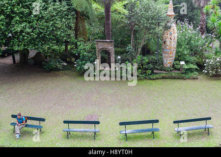 Frau sitzt alleine auf einer Bank im tropischen Garten in Funchal - Madeira. Tropischer Garten mit Bänken und einsame Frau. Stockfoto