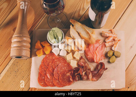 Antipasti-Platte auf der Holzoberfläche. Flasche und Glas Wein. verschiedene snacks Stockfoto