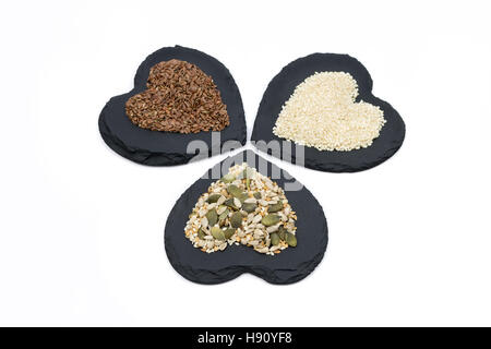 Trio von Samen, Sonnenblumenkerne, Leinsamen, Leinsamen, Kürbis und Sesam auf Herz geformt Schiefer isoliert auf weißem Hintergrund Stockfoto