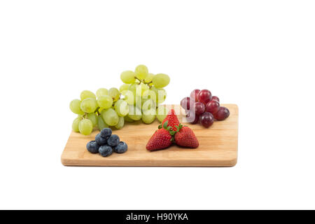 Rote und grüne Trauben, Erdbeeren und Heidelbeeren auf einem Holzbrett isoliert auf weißem Hintergrund Stockfoto