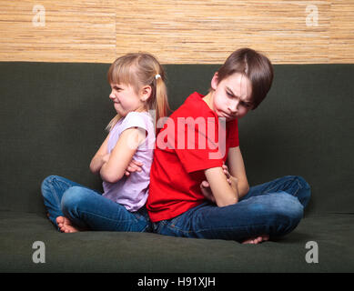 Bruder und Schwester tragen legere Kleidung auf dem grünen Sofa im Hause Arms sitzen Rücken an Rücken böse miteinander gekreuzt Stockfoto
