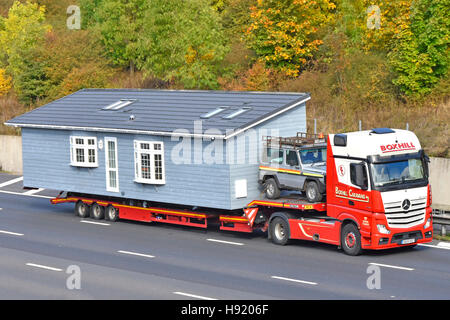 Teil der übergroßen Fabrik montiert vorgefertigten Park Home Lodge breit Ladung transportiert auf UK Autobahn lkw Tieflader Sattelzug Mit Begleitwagen Stockfoto