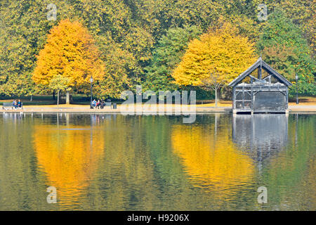 Herbstfärbung Baum und Bäume Reflexion in der Serpentine See im Hyde Park ein London Royal Park in England UK mit Sitzplätze am Gewässerrand Stockfoto