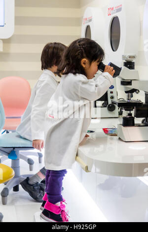 Japan, Nishinomiya, KidZania. Kinder, Junge und Mädchen in weißen Laborkittel mit Mikroskopen, kleines Mädchen auf Zehenspitzen zu belasten. Stockfoto