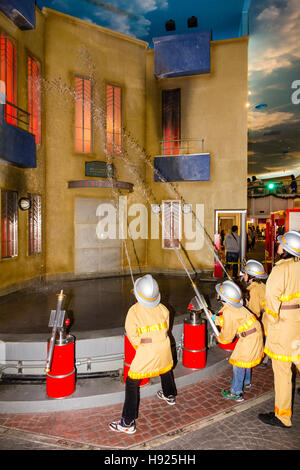 Japan, Nishinomiya, KidZania, untergeordnete Aktivität spielen. Leitung von Kindern als Feuerwehrleute, die Schläuche am brennenden Gebäude gekleidet. Stockfoto