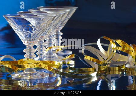 Eine Reihe von vier Cocktailgläser mit goldenen Serpentin vor blauem Hintergrund mit Reflexion Stockfoto