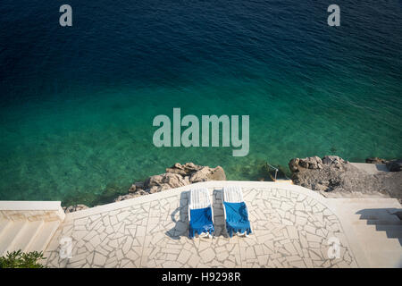 Ein Blick nach unten auf zwei Sonnenliegen auf der Terrasse von einem tiefblauen Meer in Kroatien Stockfoto