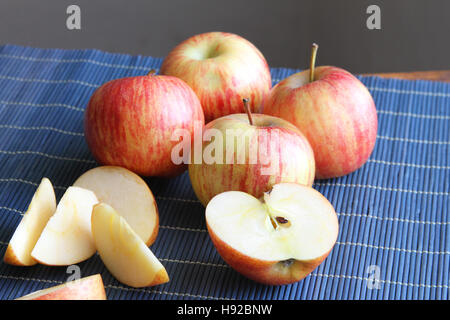 Ganze und geschnittene gestreifte rote Äpfel auf einem blauen Tischset Stockfoto