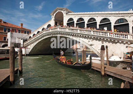 Menschenmassen auf der beliebten Rialtobrücke beobachten Touristen in einer Gondel an einem hölzernen Steg, Venedig, Italien. Stockfoto