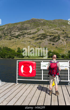 Mann mit Rucksack und Wanderschuhe steht auf Glenridding Pier, Cumbria, Blick auf die Infotafel zeigt die Namen des Fells Stockfoto