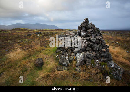 Ein Steinhaufen, einen menschengemachten Haufen (oder Stapel) von Steinen in der Wildnis Islands mit Gebirgshintergrund. Stockfoto