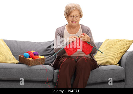 Reife Frau auf einem Sofa sitzen und stricken isolierten auf weißen Hintergrund Stockfoto