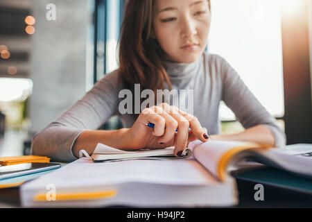 Schließen Sie herauf Bild an einer jungen Studentin tun Aufgaben in Bibliothek. Asiatische Frau Notizen aus Lehrbüchern. Stockfoto