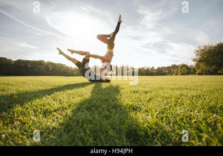 Gesunde junge Paar Acro Yoga auf dem Rasen zu tun. Mann und Frau verschiedene Yogastellungen paarweise im Freien im Park zu tun. Stockfoto