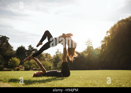 Fit paar tun akrobatische Yoga üben im Park. Mann auf dem Rasen liegen und Frau balancieren. Stockfoto