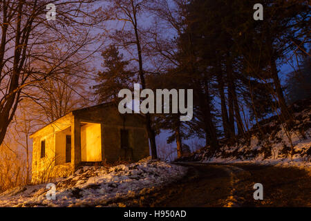 Wunderschön beleuchtet Dorfhaus im Wald gegen gelbe Straßenlampen.  Winter-Berg-Szene Stockfoto