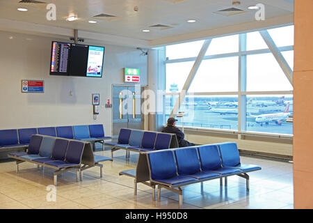 Ein einsamer Passagier wartet im Abflugbereich im Terminal des Flughafens Gatwick Nord. Sitzt, starrte aus dem Fenster auf Flugzeuge. Stockfoto