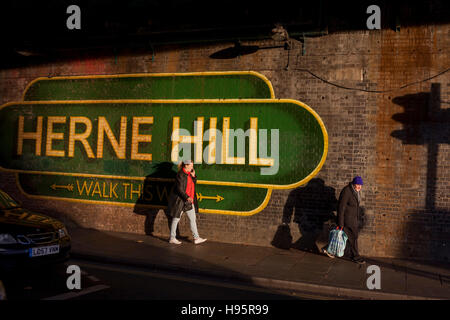 Fußgänger laufen unter dem großen Schild unter der Eisenbahnbrücke, Herne Hill, South London Lambeth SE24 ankündigt. Stockfoto