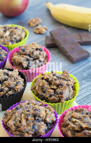 Obst-Muffins auf einem gelben Serviette und einem grauen Holztisch. Apfel, Banane, Walnüsse und Schokolade im Hintergrund. Stockfoto