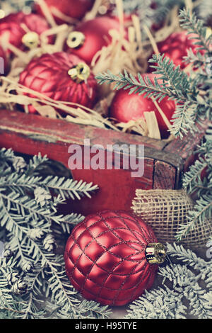 Glas Christbaumschmuck verpackt in einer alten antiken Holzkiste mit Schnee bedeckten Kiefer Ästen um sie herum. Stockfoto