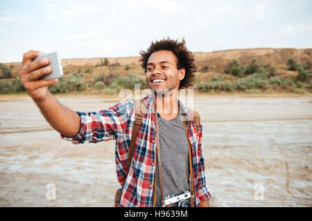 Glücklicher afroamerikanische Mann stehen und nehmen Selfie mit Handy im freien Stockfoto