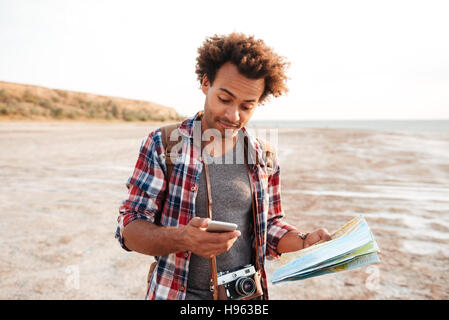 Hübschen afrikanischen jungen Mann mit Karte und Vintage-Foto-Kamera mit Handy im freien Stockfoto