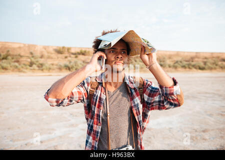 Ernsthafter afrikanischer jungen Mann bedeckt Kopf mit Karte und am Handy im freien sprechen Stockfoto