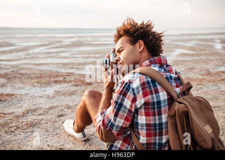 Konzentriert afroamerikanischen jungen Mann mit Rucksack sitzt und die Pistures im freien Stockfoto