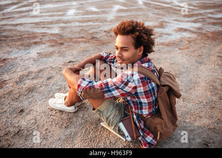 Hübscher nachdenklich afrikanischen junger Mann mit Rucksack sitzen und denken Stockfoto