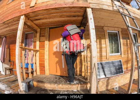 Mädchen-Backpacker kommt in einem Holzhaus im Wald auf der Veranda. Stockfoto