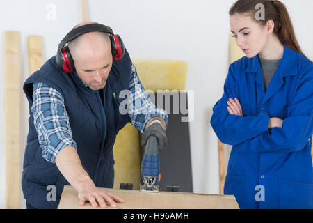 Tischler mit weiblichen Auszubildenden Hobeln Holz in Werkstatt Stockfoto