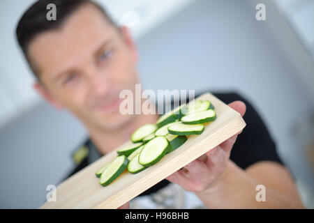 Mann mit in Scheiben geschnittenen Gurken Verlegung auf ein Schneidbrett aus Holz Stockfoto