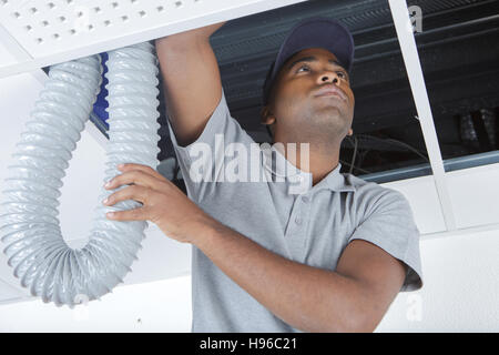 junge männliche Elektriker auf Trittleiter Rohre in der Decke installieren Stockfoto